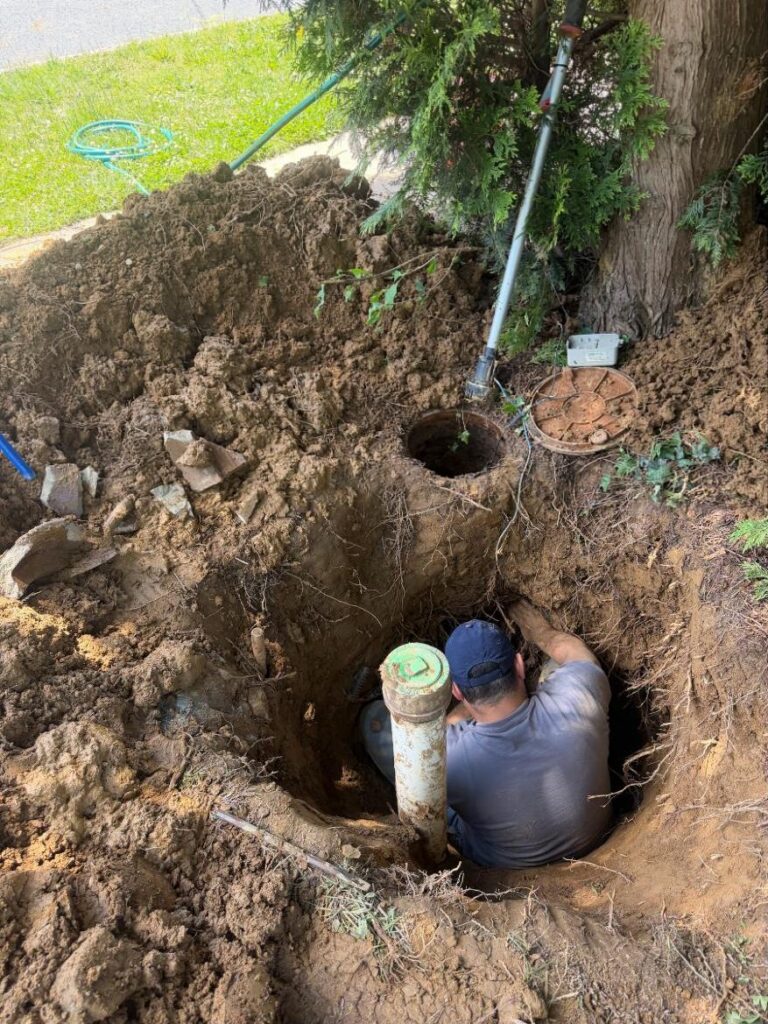 Plumber in an excavated pit repairing a sewer cleanout